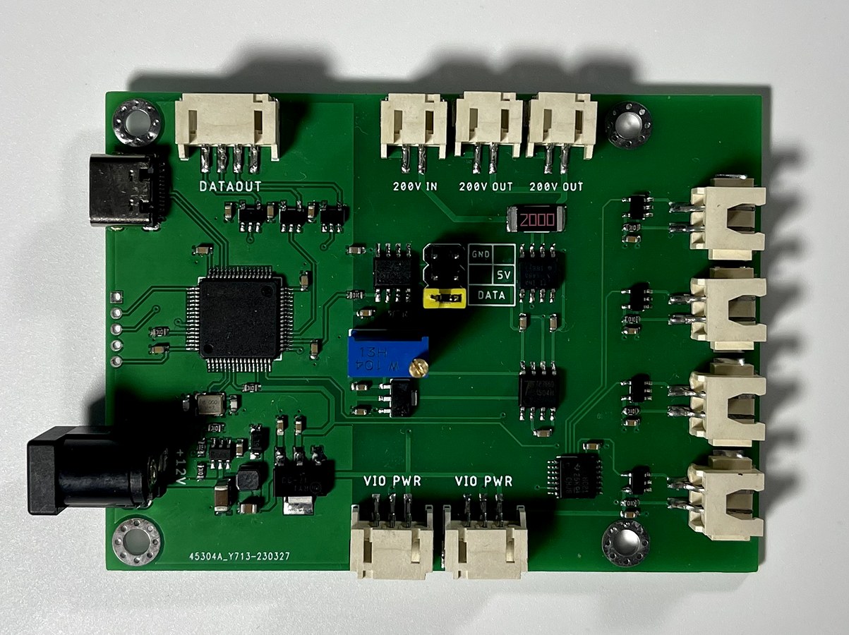The driving board: a green circuit board with a microcontroller, a 200 volt input and two 200 volt outputs, data and power connectors, and rows of sockets that route stimulation and sensing to the textile's electrodes.
