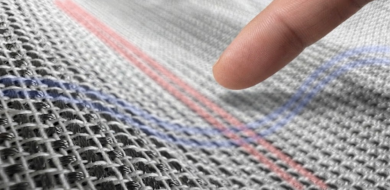 A close-up of the woven textile with a fingertip touching it. Overlaid red and blue lines run through the weave, tracing the conductive yarns that form patterns on the fabric.